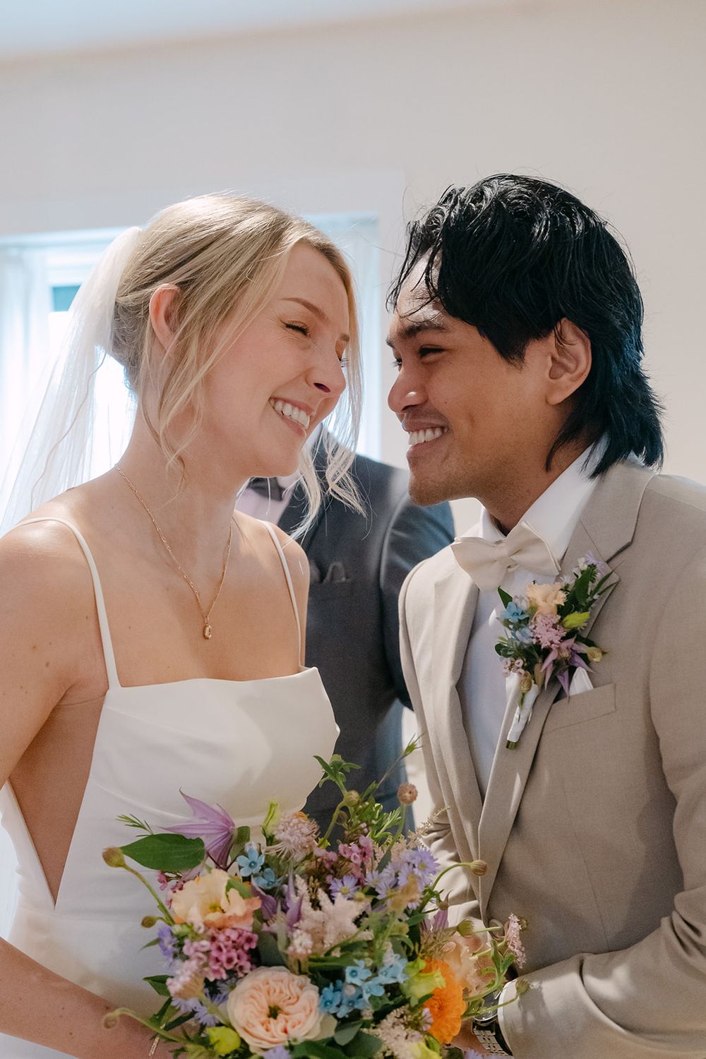 A happy couple shares joyful laughter and intimate moments during their wedding photoshoot with colorful floral bouquets.