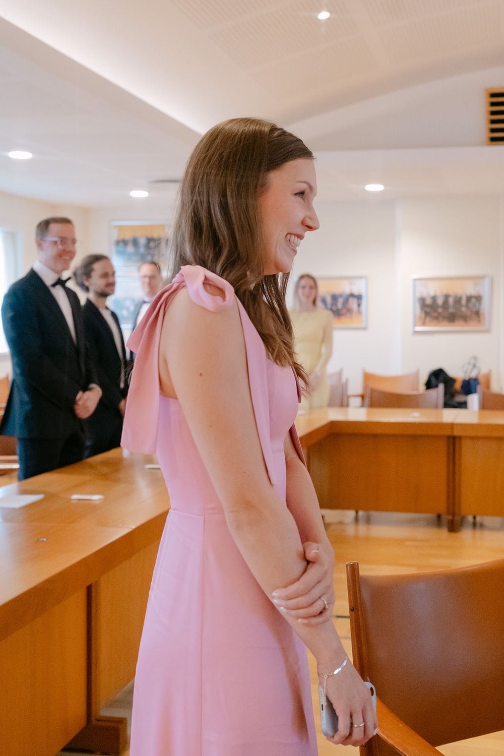 A person in a pink dress stands at a wooden counter in what appears to be an office or courthouse setting.