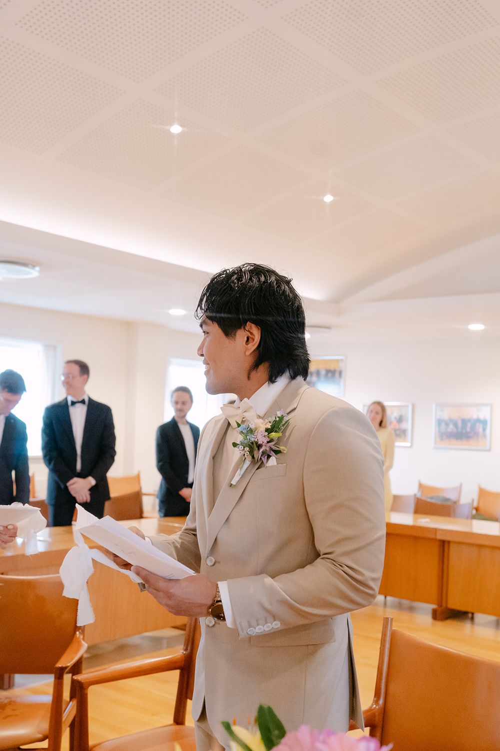 Two people in light colored suits stand together during an indoor ceremony.