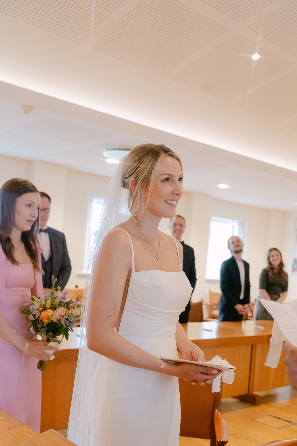 Wedding guests gather in a bright modern room with wooden podiums and white decor.