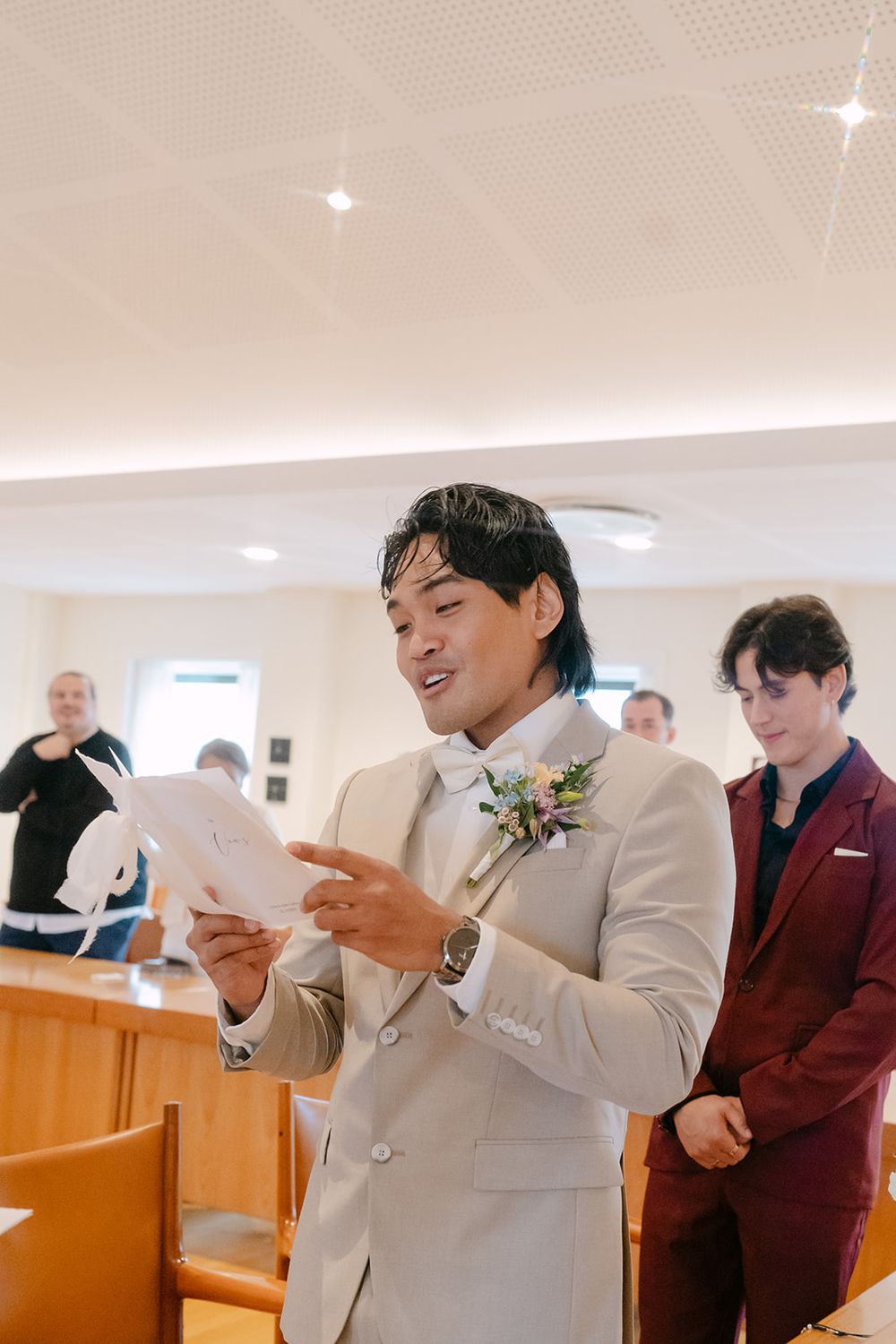Two people in light suits stand next to each other looking at papers during what appears to be a formal ceremony.
