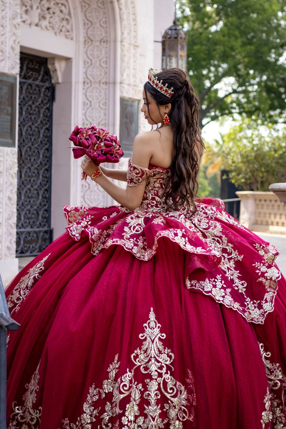 Back view of an ornate magenta and white lace quinceañera dress with floral bouquet.