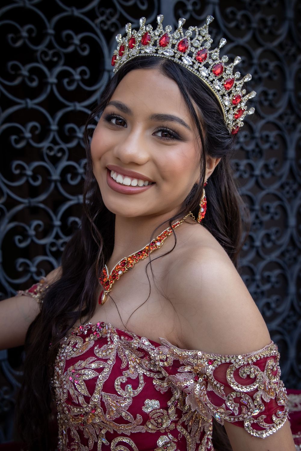 Close-up shots of a burgundy and silver embellished gown with matching crown against an ornate iron gate background.