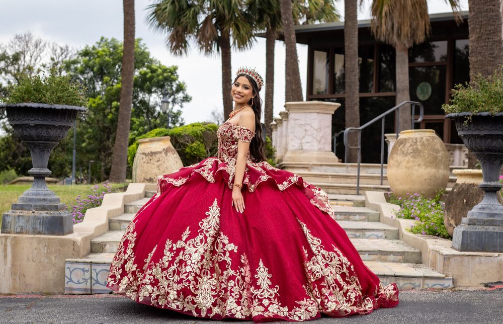Red formal gown with silver embroidery photographed against architectural elements and palm trees.