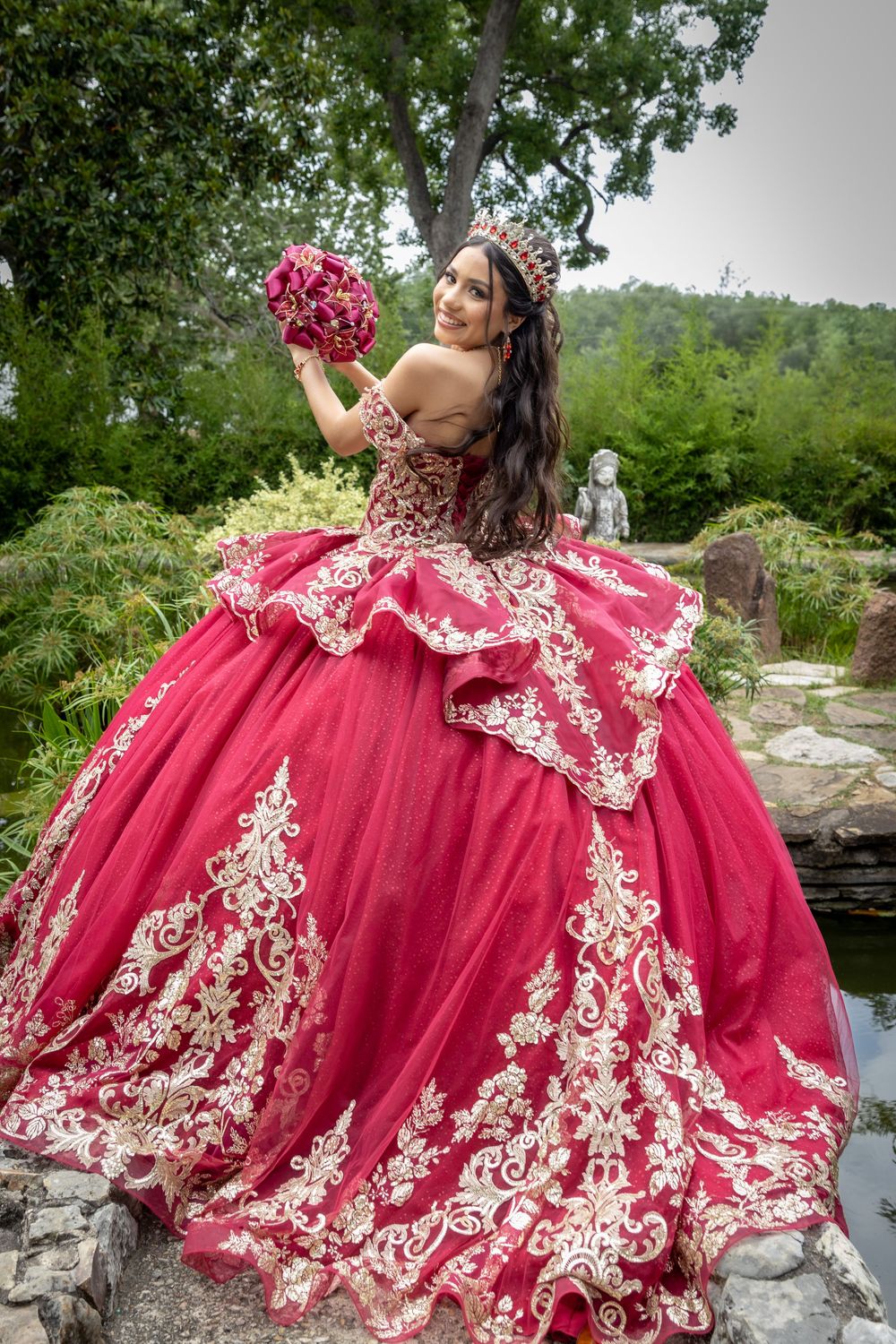 Dramatic red and gold embellished ball gown photographed outdoors against natural stone landscaping.