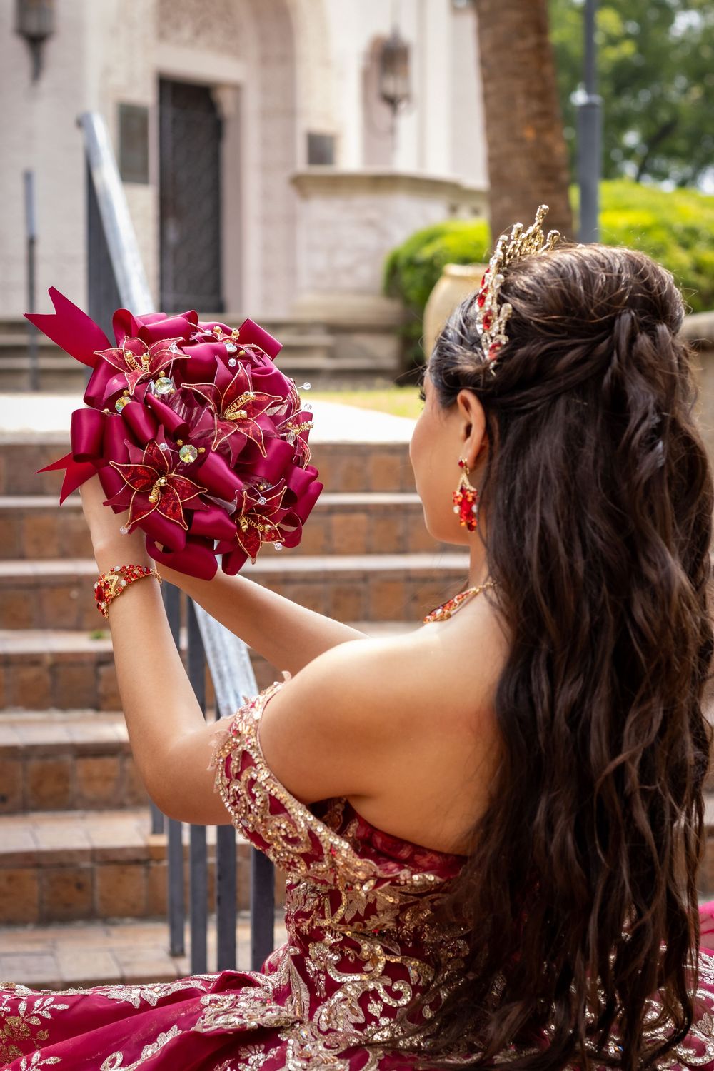 A burgundy bouquet matches an elegant embroidered dress as shown from behind on church steps.