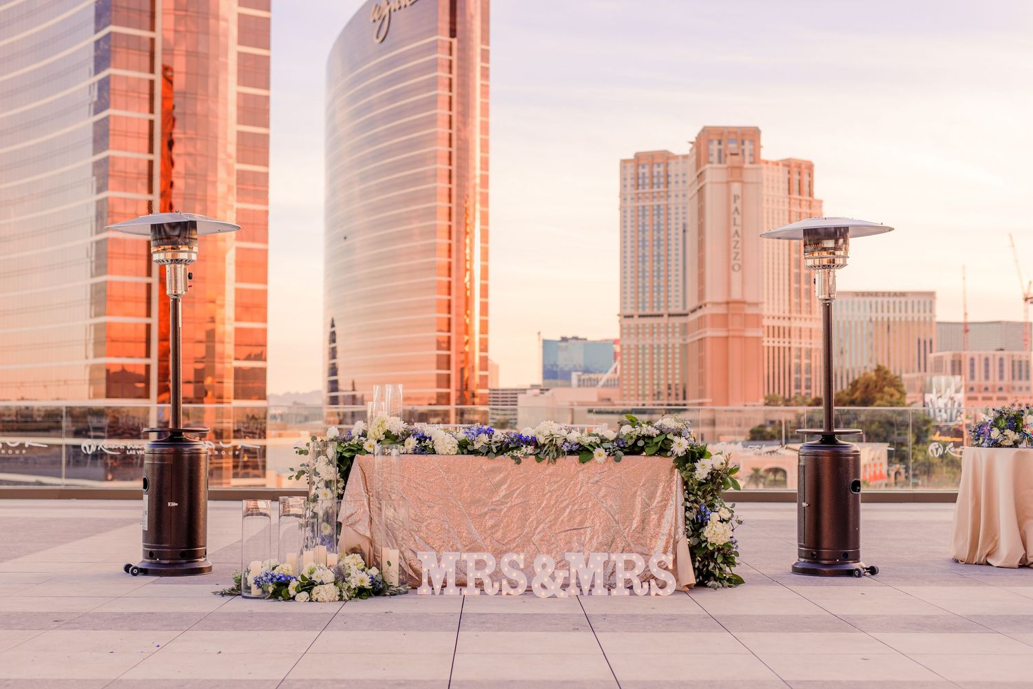 Rooftop wedding sweetheart table with MRS&MRS sign, floral arrangements, and Las Vegas skyline backdrop at golden hour at Resorts World.