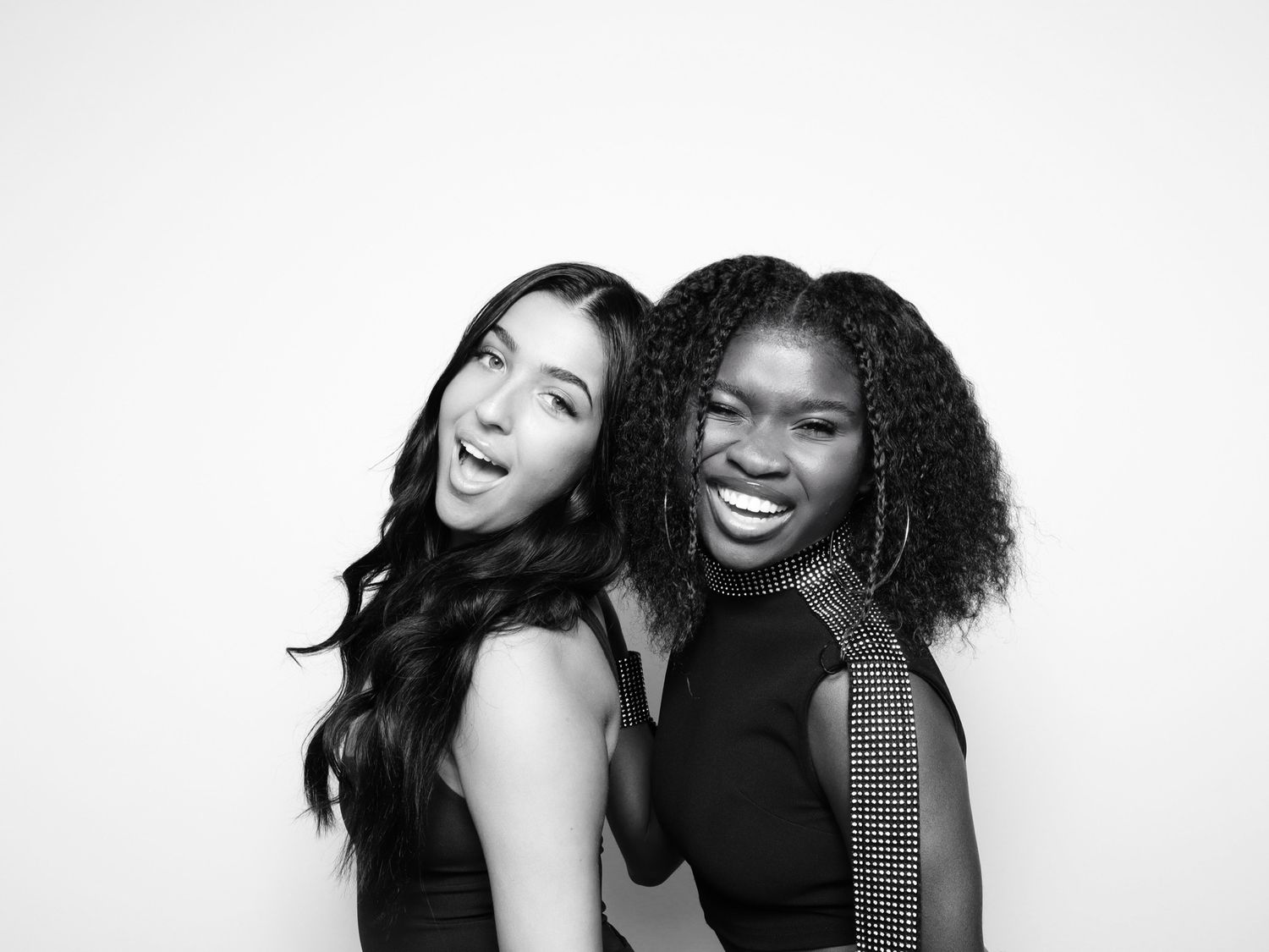 Two friends in black outfits laugh and pose together for a black and white portrait in a event photo booth.