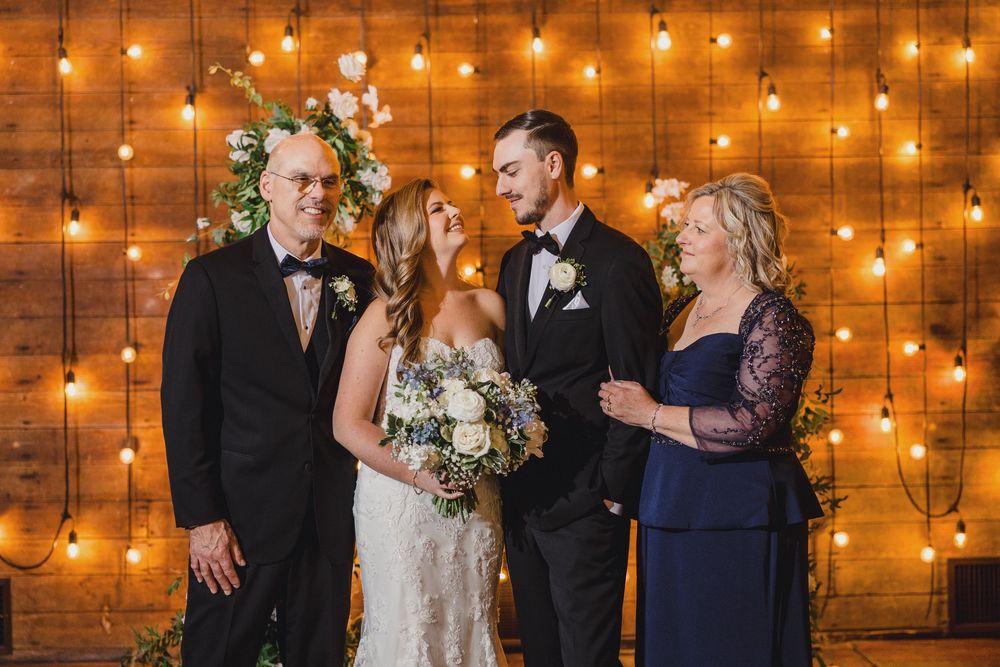 Wedding party celebrating under warm string lights against rustic wooden walls.