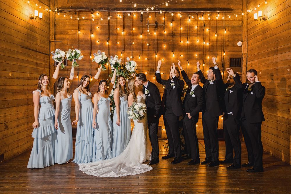 Wedding ceremony group shot in a rustic barn venue with warm lighting and wooden walls.