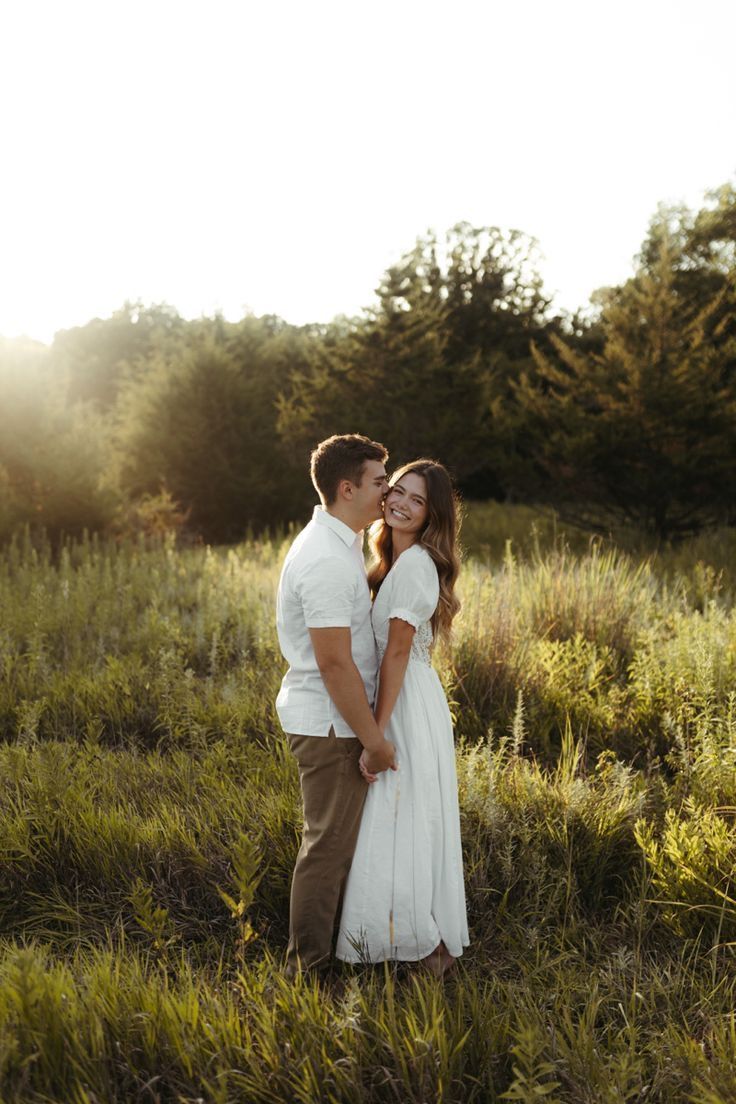 A romantic couple embraces in a sunlit meadow at golden hour, surrounded by tall grass and trees.