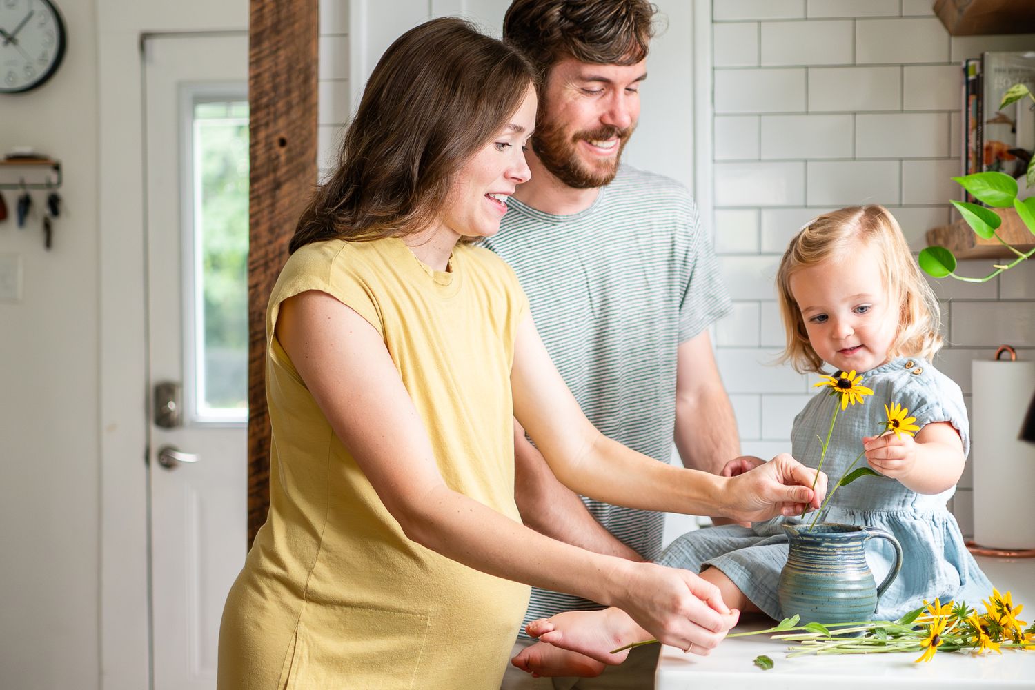 A family arranges flowers together by their kitchen sink during an at-home family photo shoot.