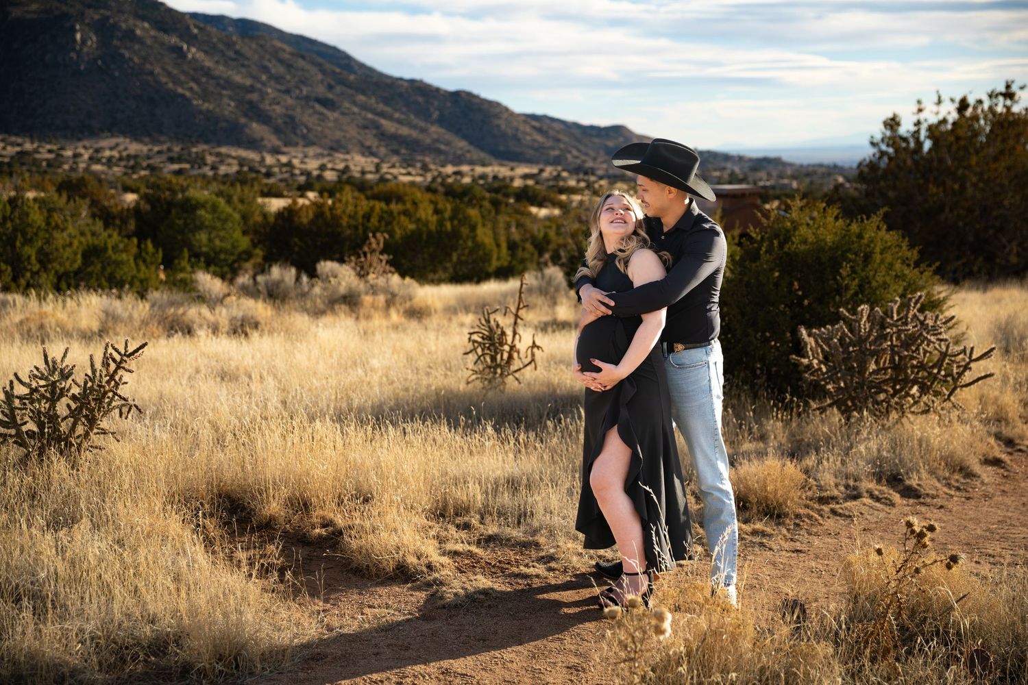A couple embraces in a desert landscape with golden sunlight and desert plants during a romantic photoshoot.