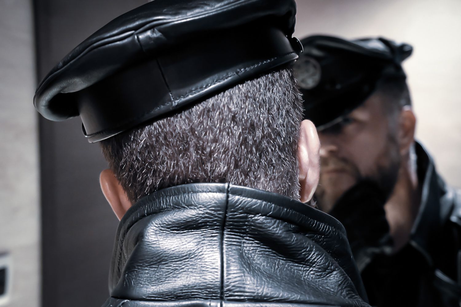 Close-up rear view of a man in a black leather cap and jacket reflected in a mirror.
