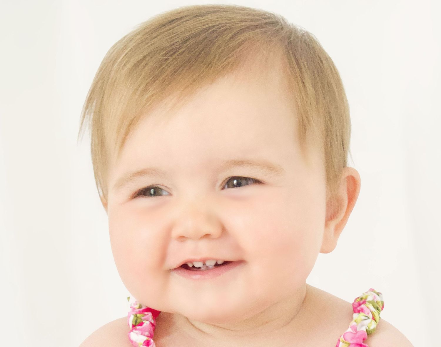 Close up portrait of smiling baby wearing floral necklace.