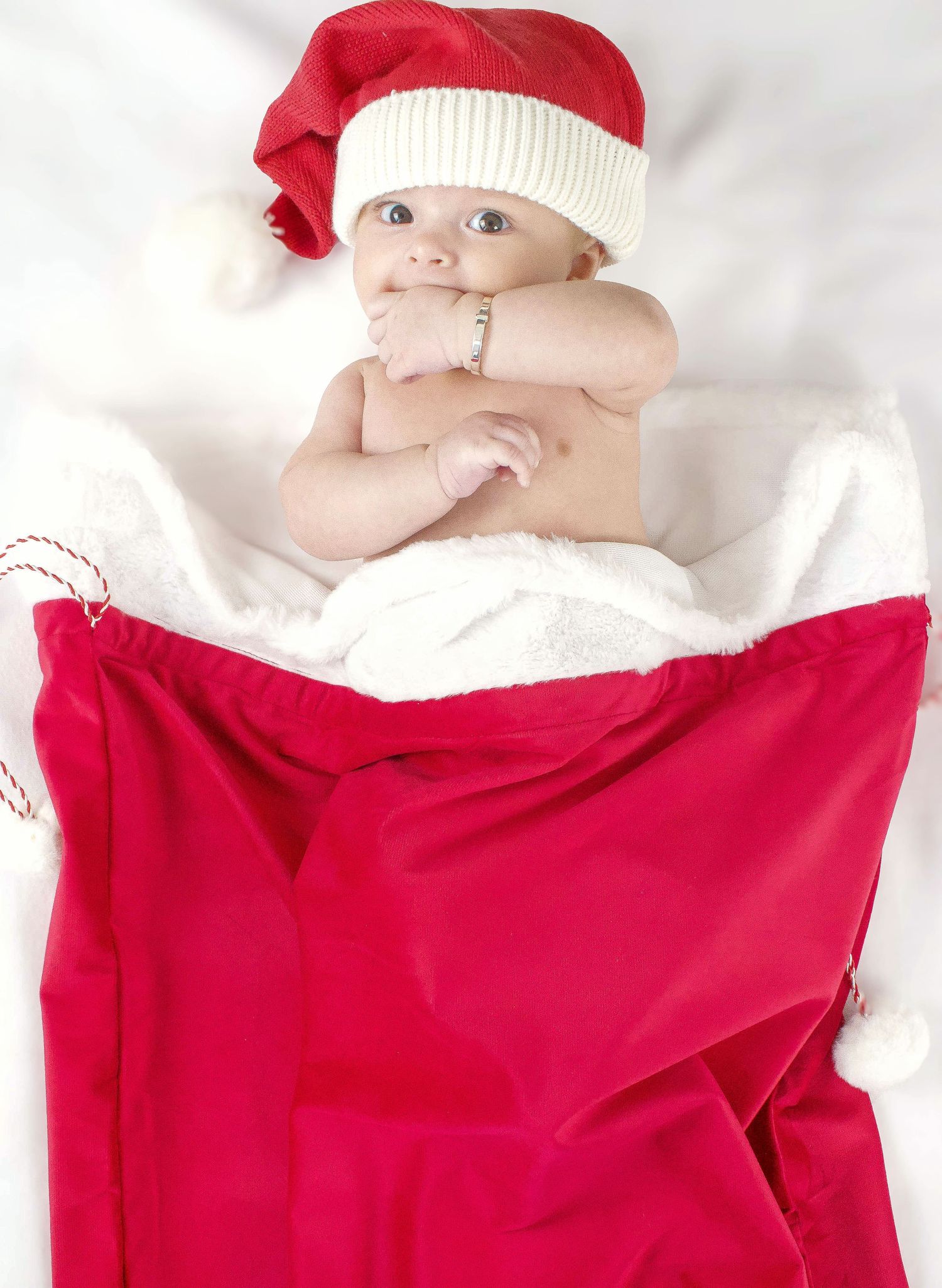Baby in red Santa hat and blanket on white background for holiday portrait.