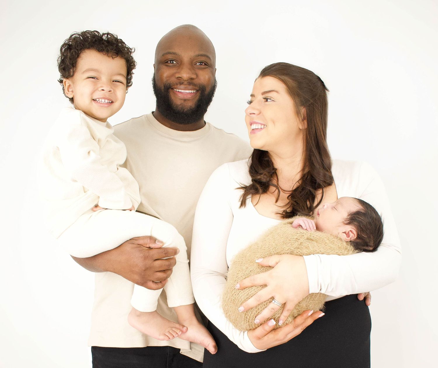 Family wearing coordinated white and cream outfits posing together against white background.