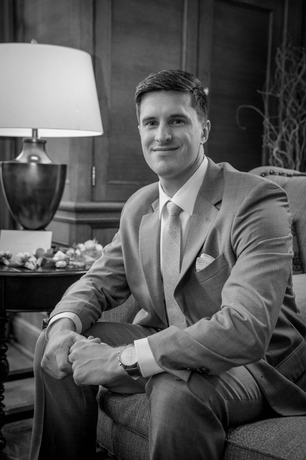Classic black and white portrait of a groom in a light colored suit sitting in an elegant room.