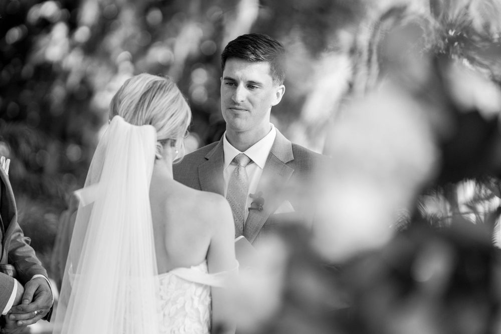 Intimate black and white wedding ceremony moment captured through blurred foreground elements.