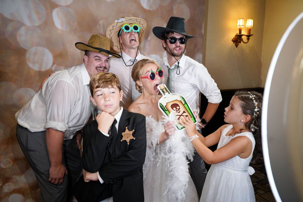 Fun photo booth moment with wedding party wearing hats and props against a bokeh background.