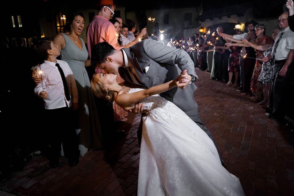 Dynamic night shot of wedding guests performing a group dance move on brick patio.