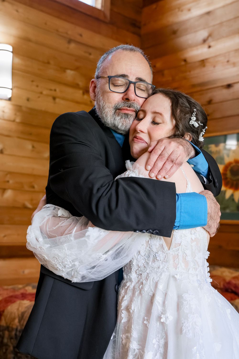 Emotional embrace between a bearded figure in black suit and person in white lace wedding dress in a rustic wooden setting.