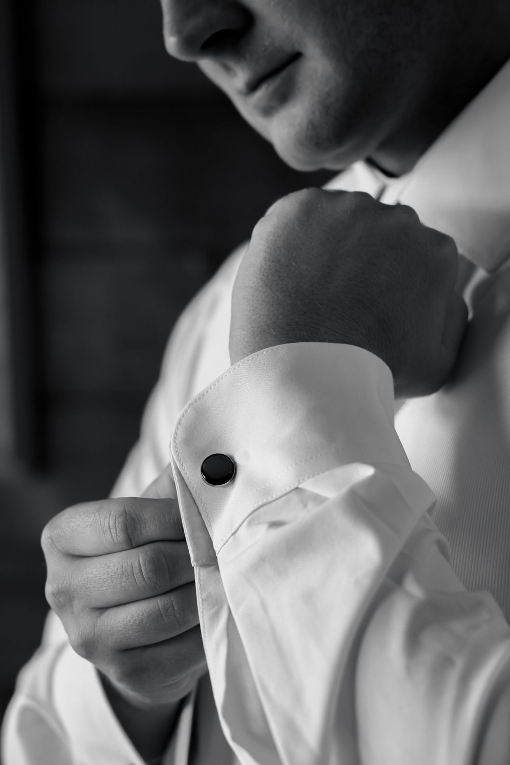 Close-up black and white photo of someone adjusting a formal shirt cuff with cufflink.