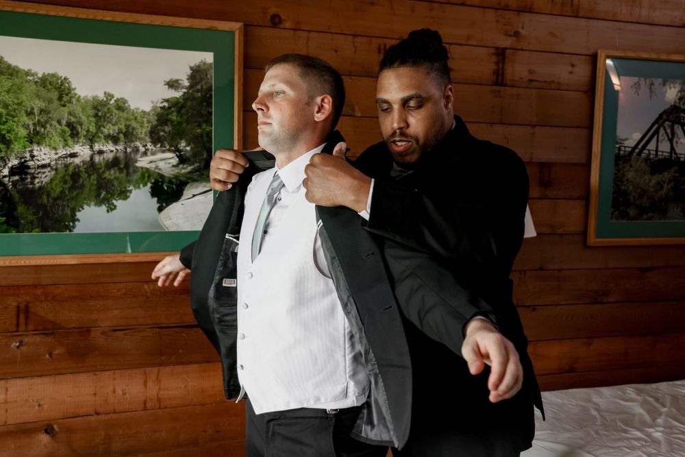 Two people in formal attire helping with wedding day preparations in a rustic setting.