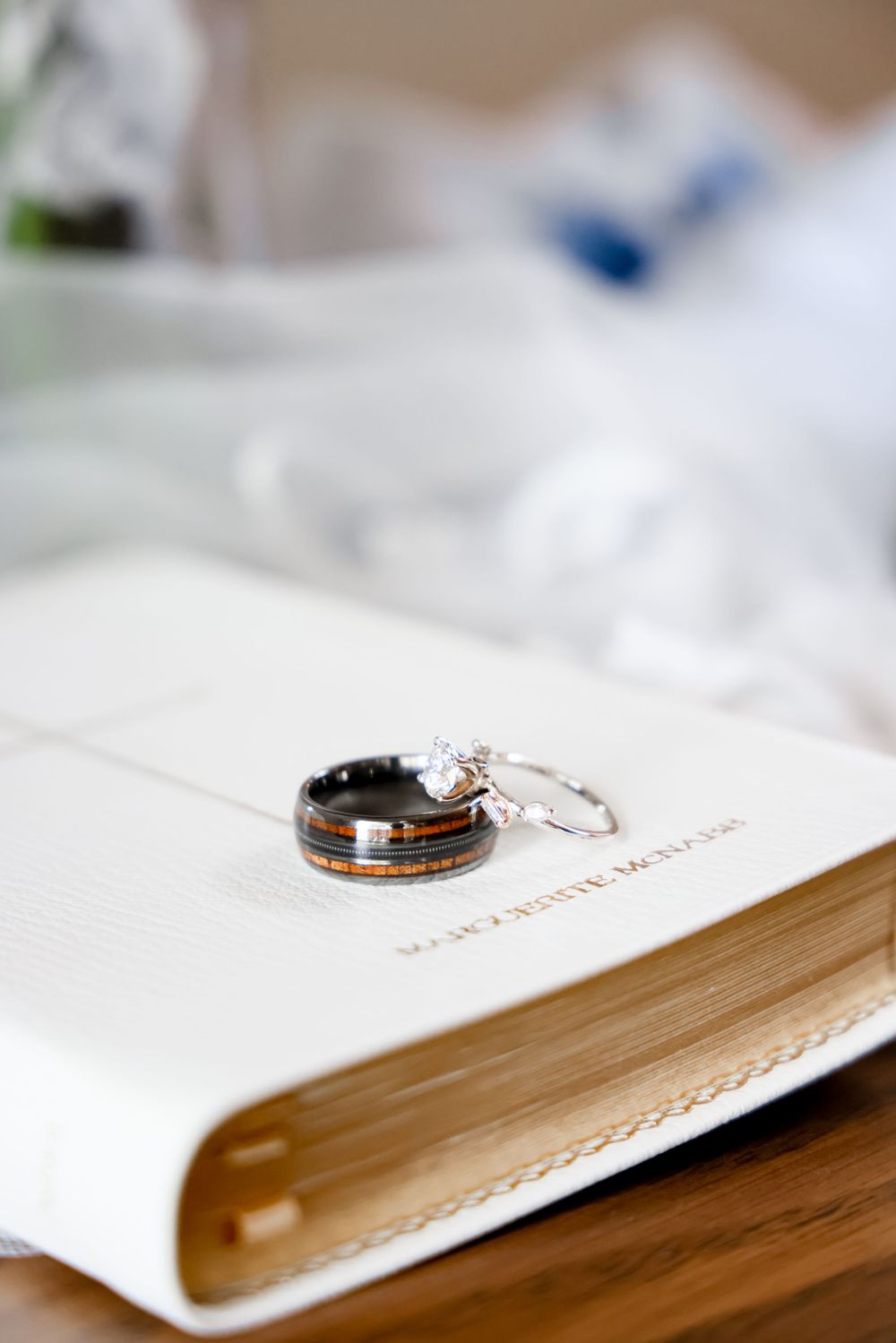 Wedding rings resting on a white paper or book with elegant typography visible underneath.