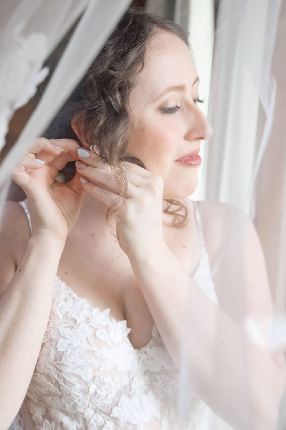 A serene moment captured of someone in a white lace wedding dress getting ready by a window.