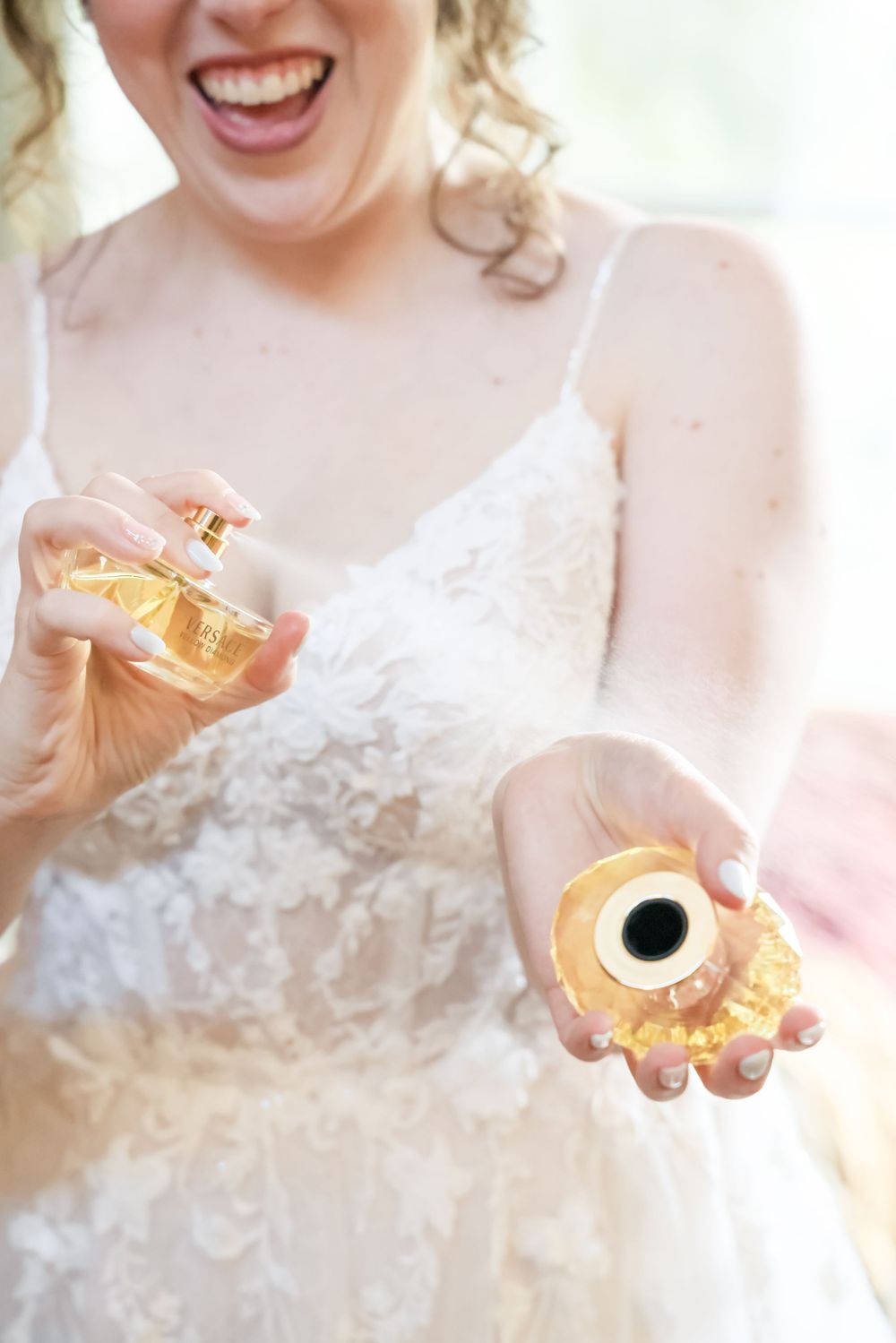 Close up of hands holding perfume bottles while wearing a detailed lace wedding dress.