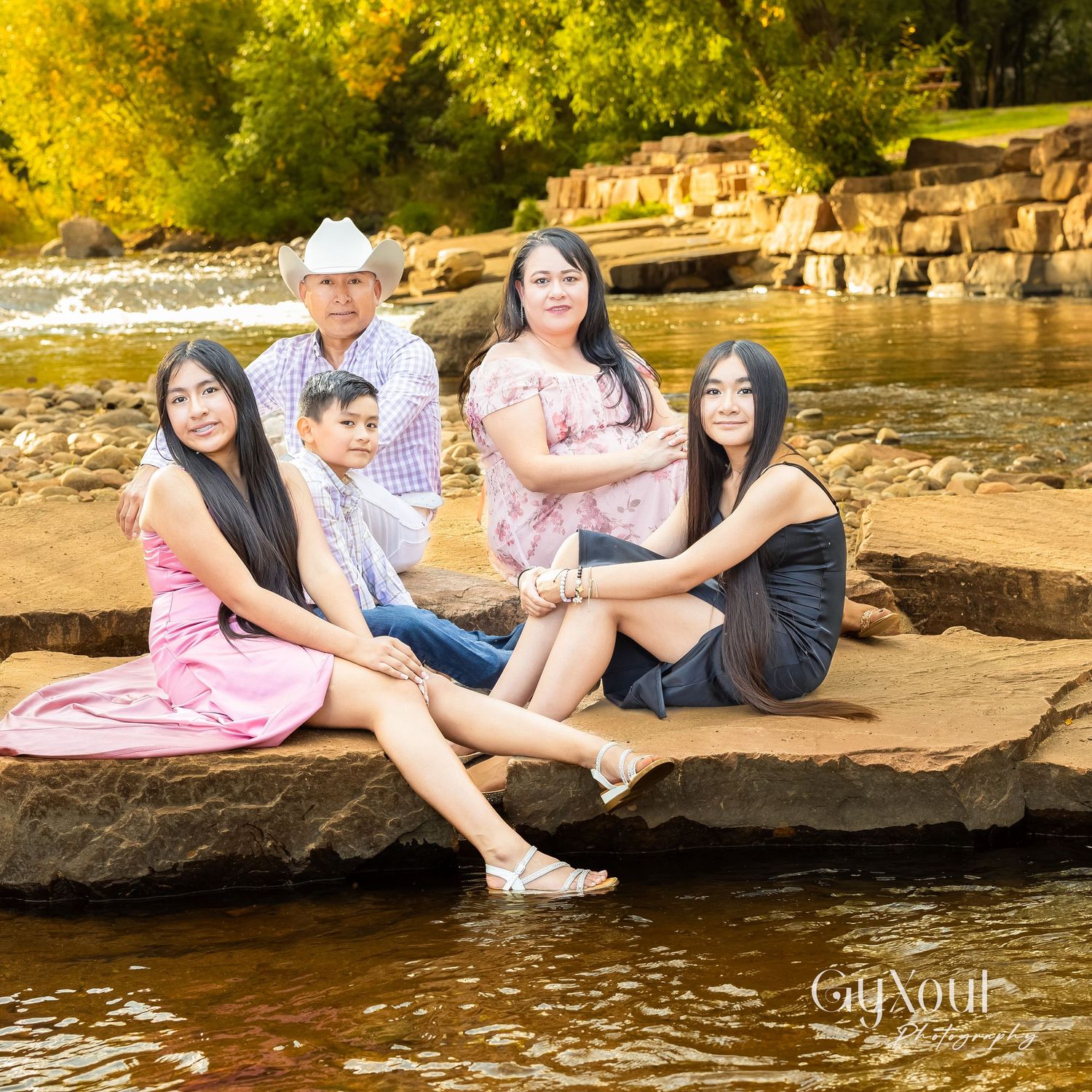 Family group sitting on rocky riverbank during golden hour photo session.