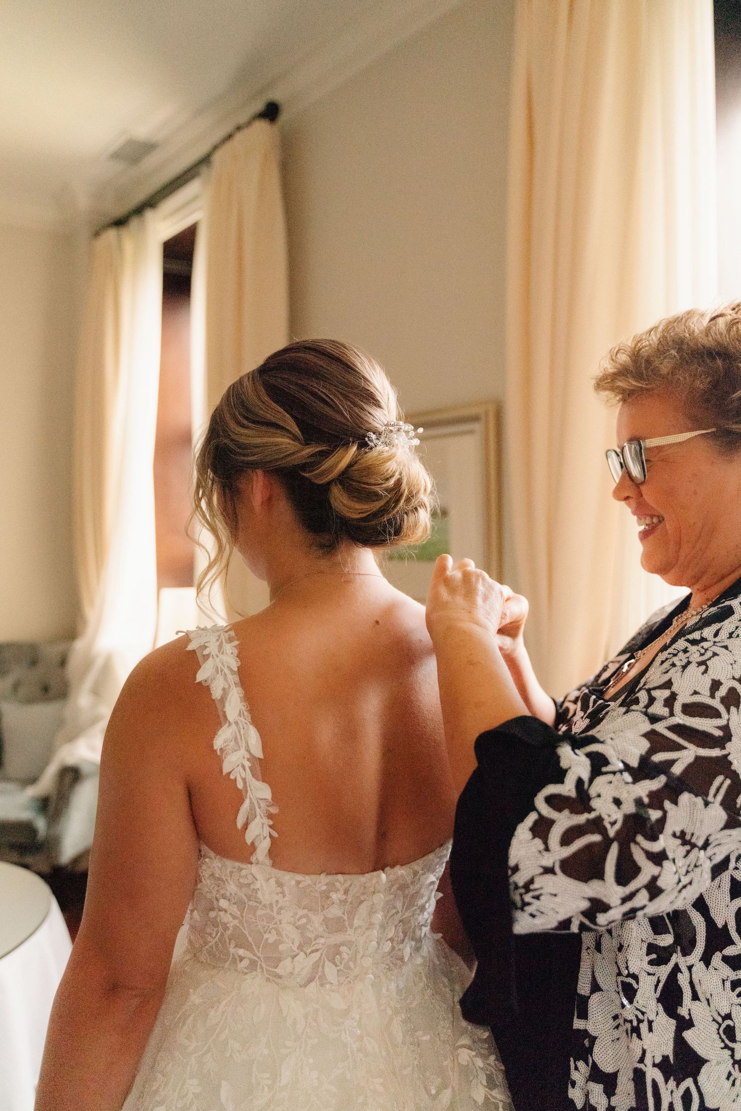 A wedding dress being adjusted in a room with cream curtains and natural lighting.