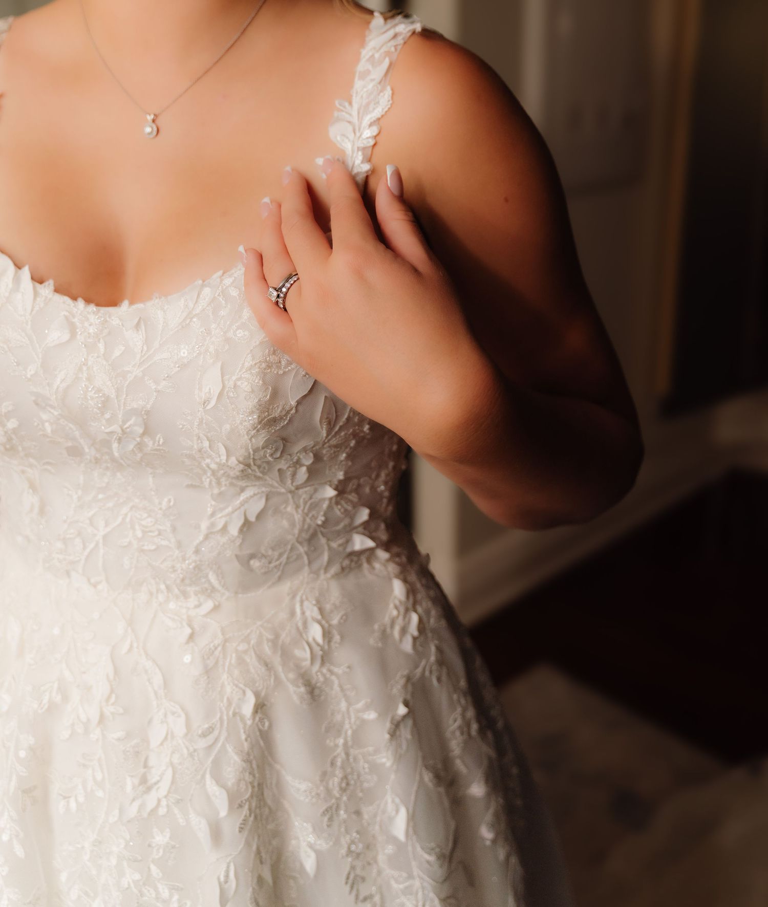 Close-up detail of a white lace wedding dress bodice with delicate embellishments and a small necklace.
