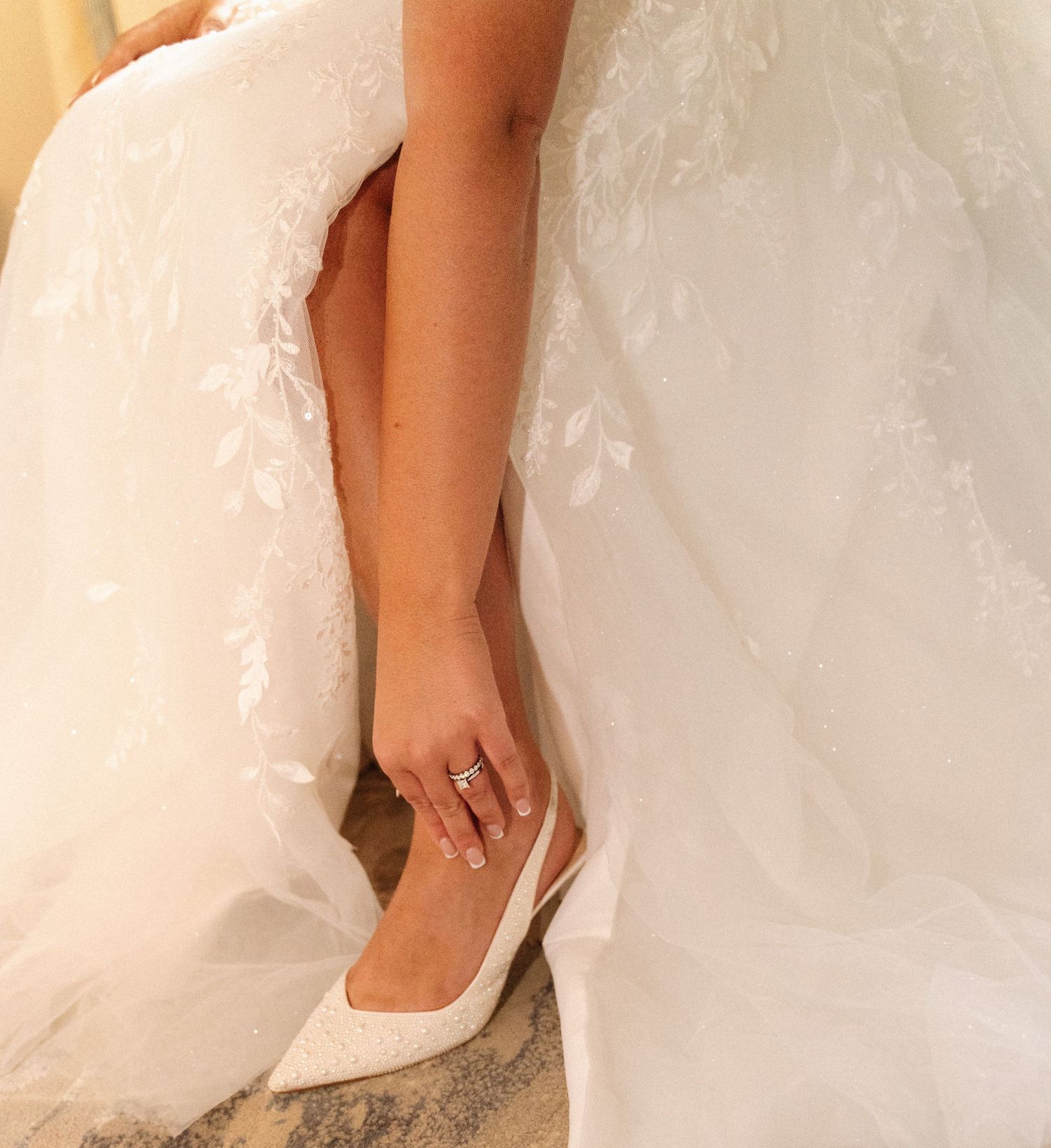White bridal shoe peeks out from beneath layers of delicate wedding dress fabric.