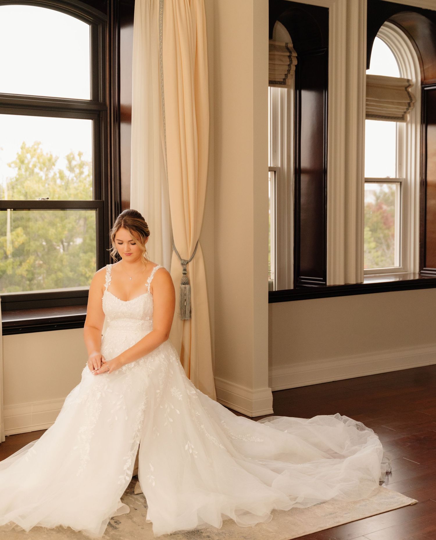 An elegant wedding dress with a flowing train creates a stunning silhouette against large arched windows.