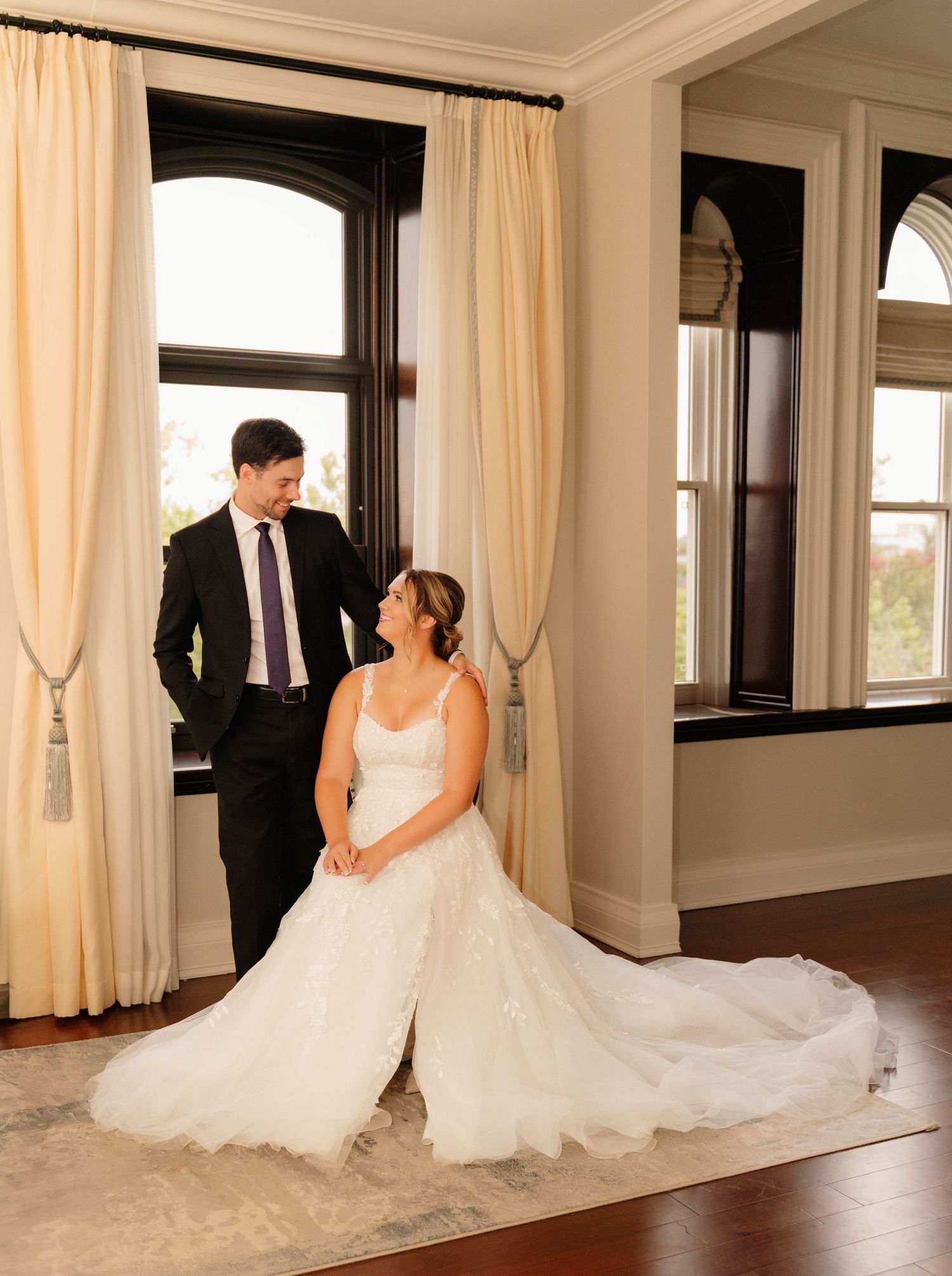 Elegant wedding portrait in a room with tall windows and cream curtains.