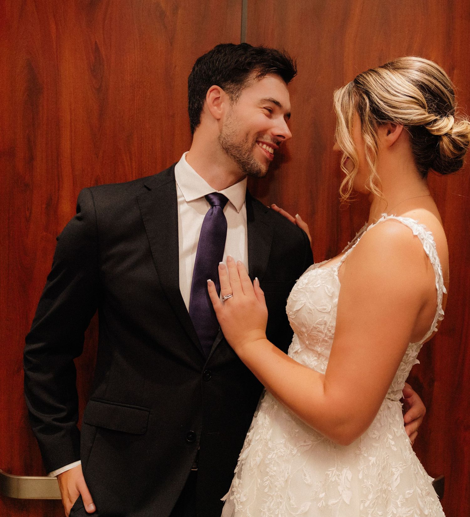 Wedding couple shares a tender moment against a wooden wall background.