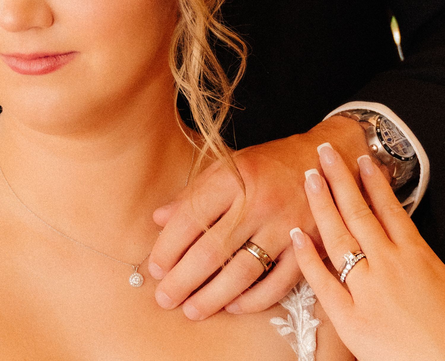 Close-up of hands with wedding rings and delicate lace dress details.