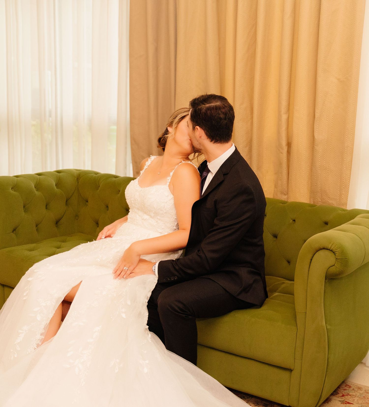 Romantic wedding portrait of couple sharing tender moment on vintage green sofa.