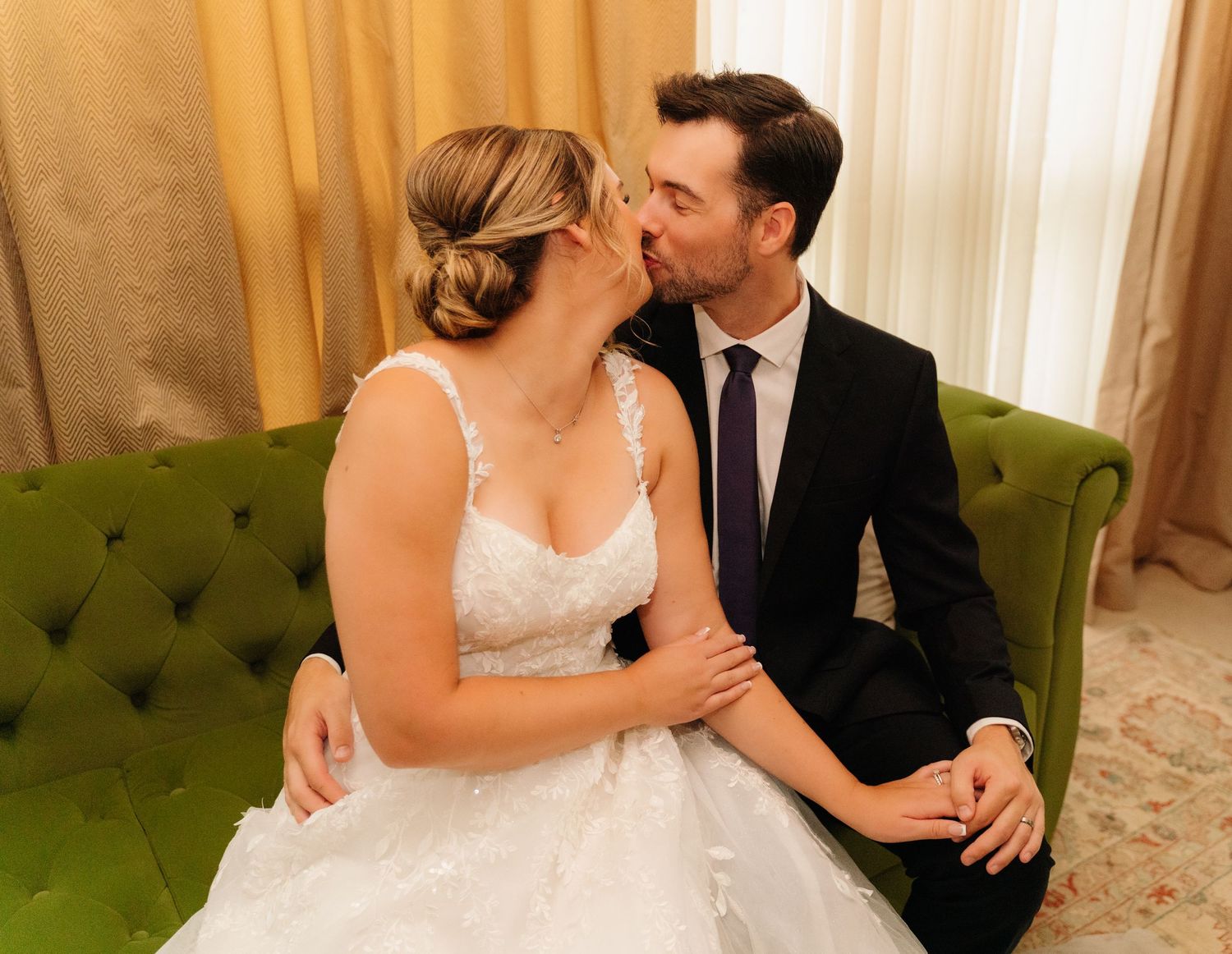 Intimate wedding moment captured on green tufted sofa in elegant room setting.