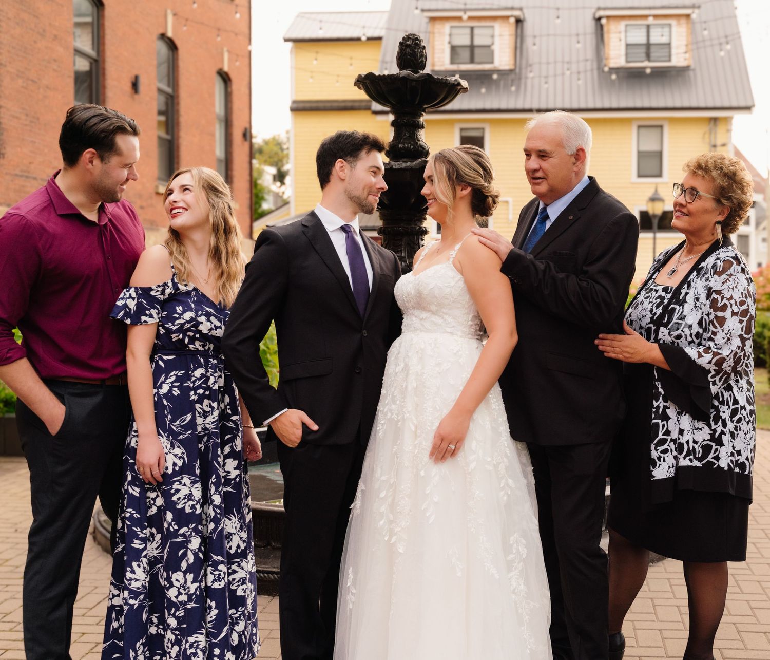 Candid wedding party group shot with laughter by outdoor fountain.