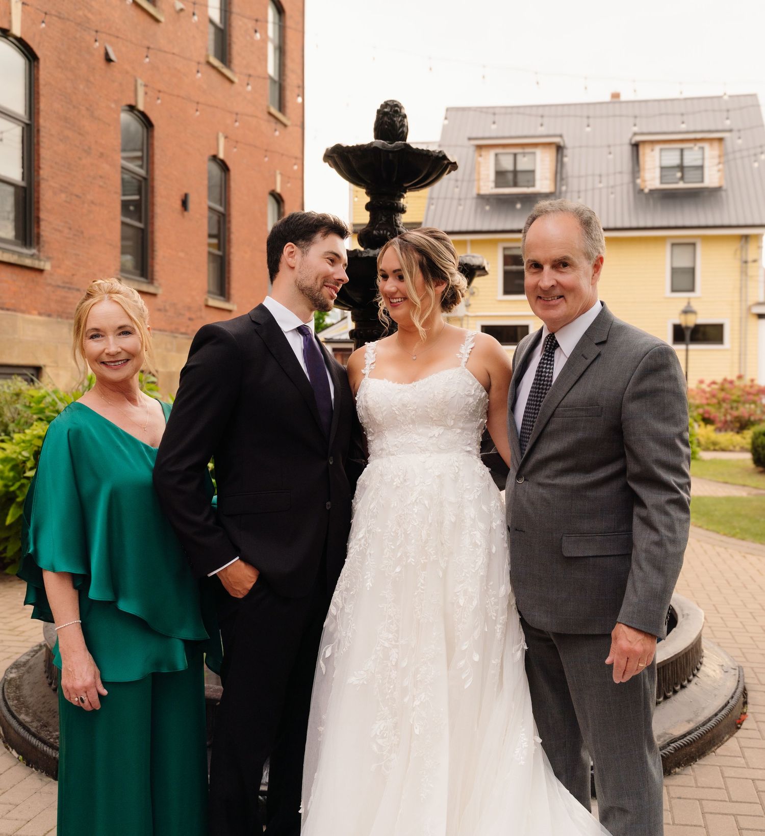 Small wedding party poses together by ornate black fountain outdoors.