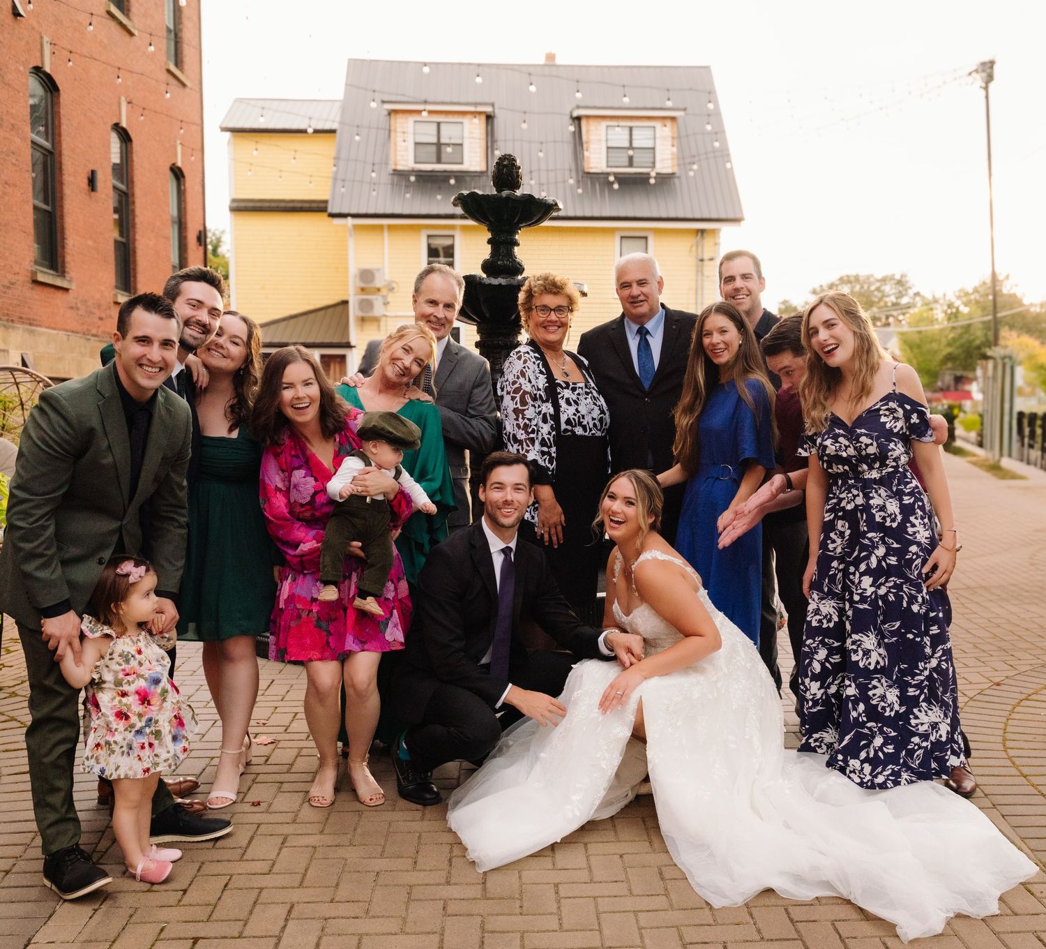 Casual wedding photo with party members in colorful attire by brick building.