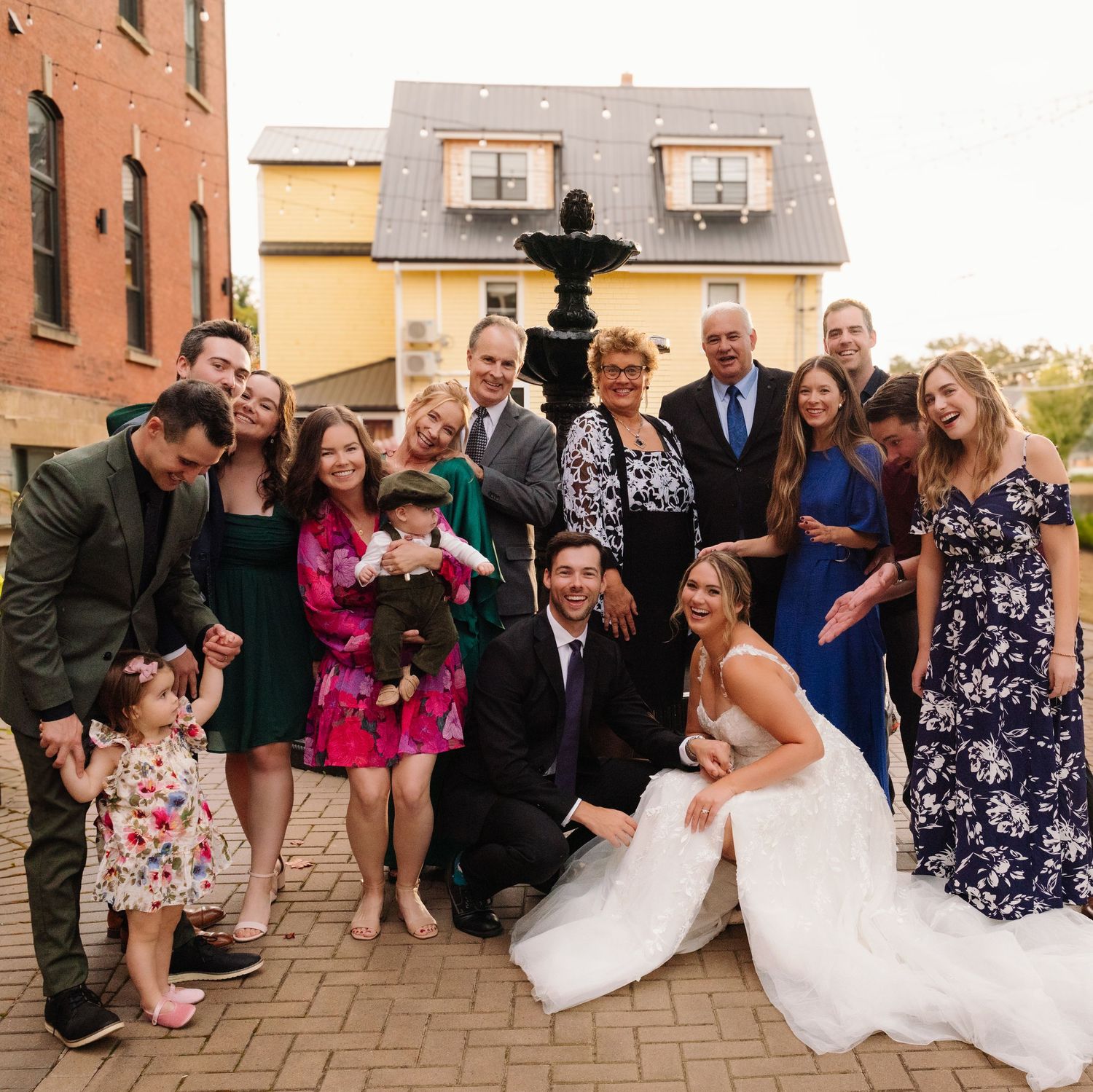 Fun wedding group shot with party members gathered around fountain outdoors.