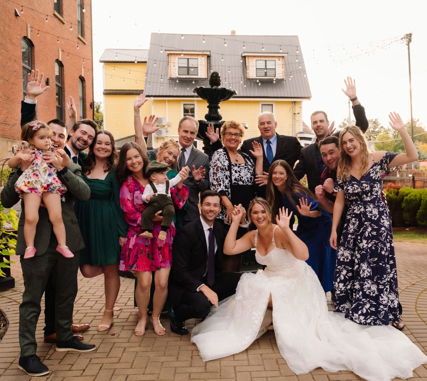 Energetic wedding party photo with group waving and celebrating outdoors.