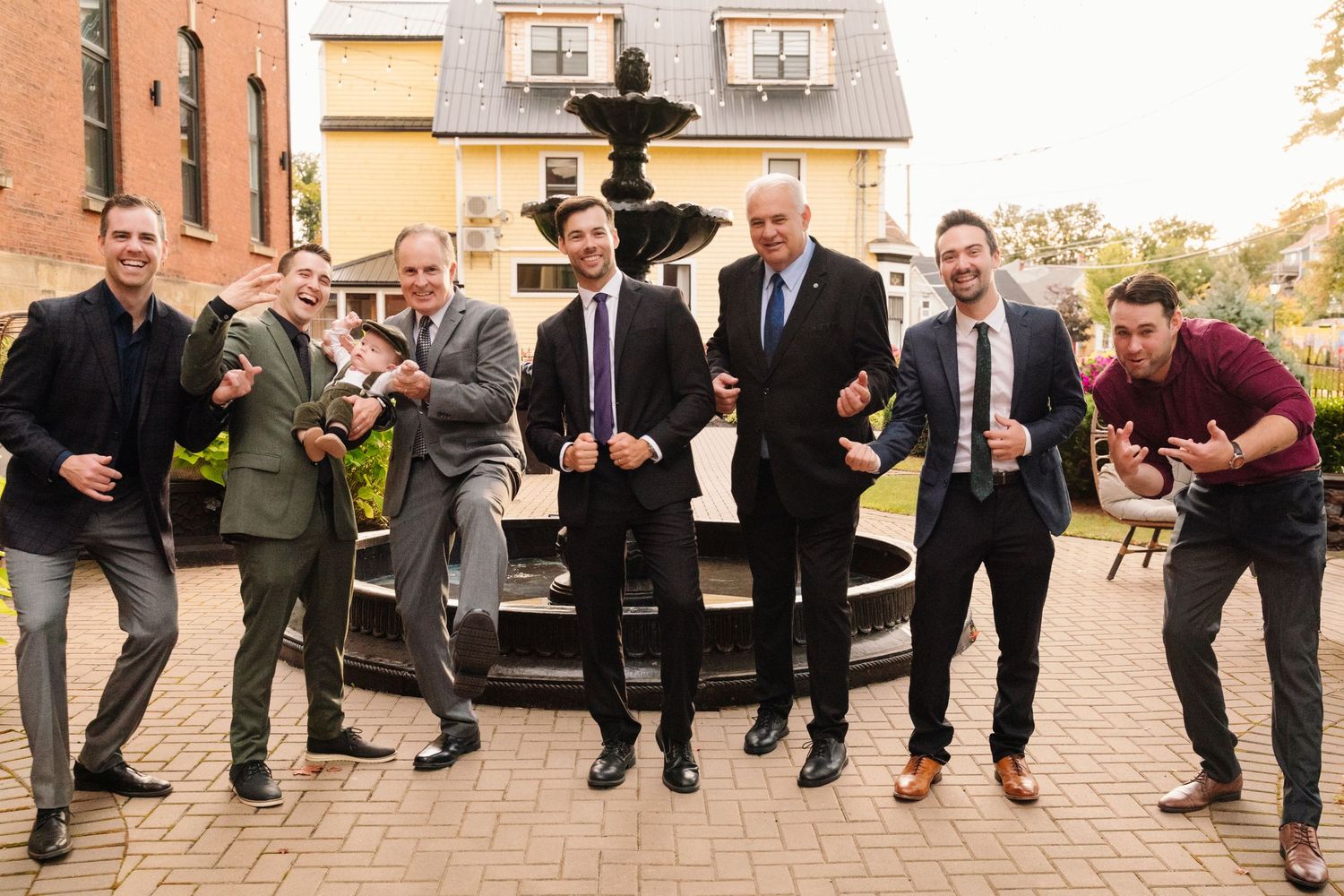 Wedding party members strike fun action poses near outdoor fountain.