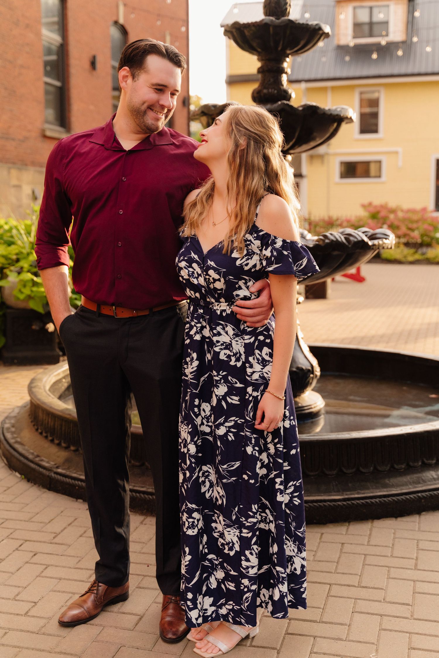 Romantic couple embraces and laughs near decorative water fountain.