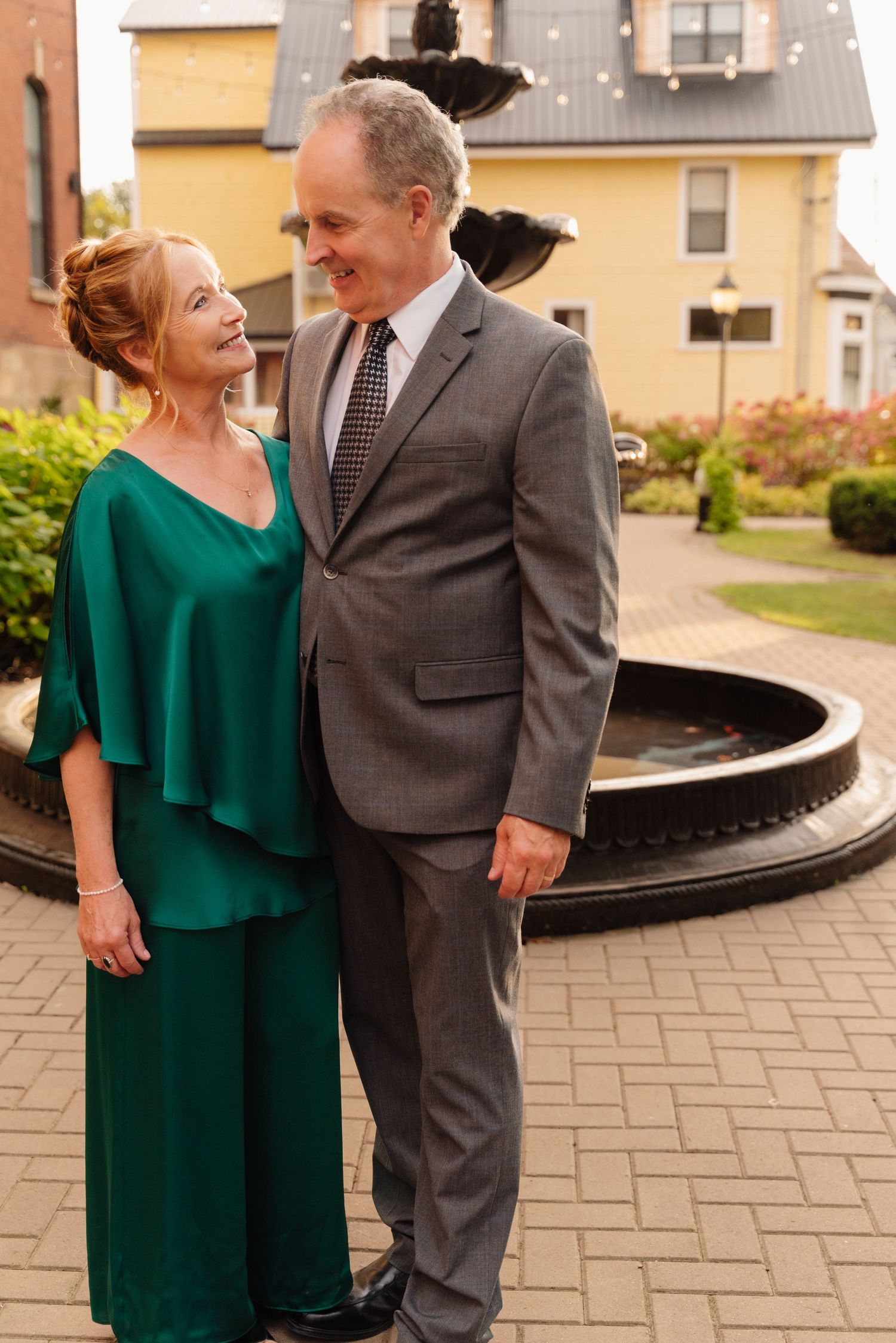 Couple in formal attire shares intimate moment by fountain wearing emerald green and grey.