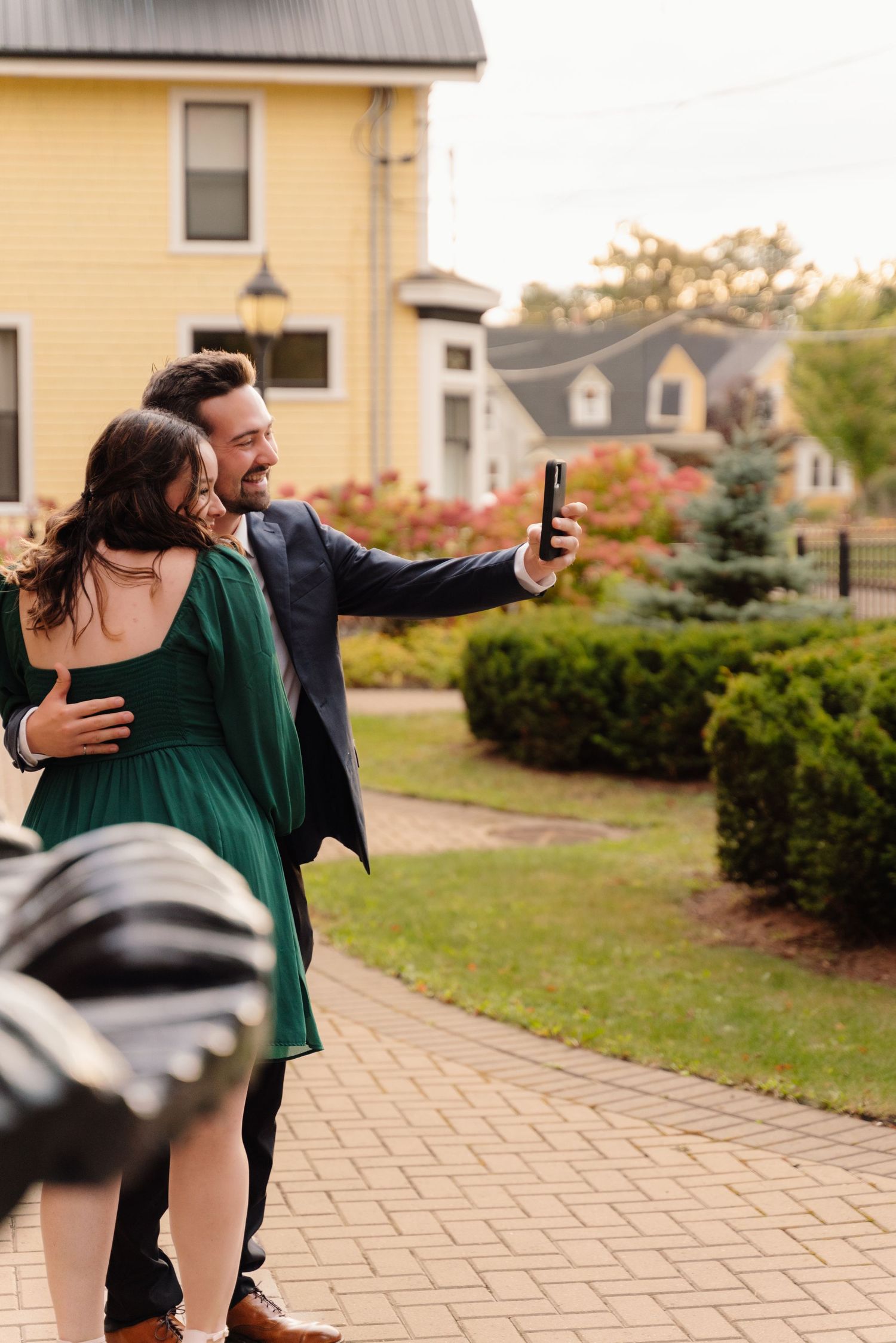 Couple taking selfie together on brick pathway near yellow building.